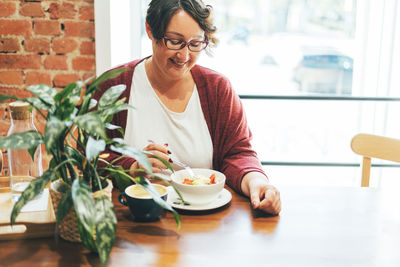 Adult smiling brunette woman in glasses in casual clothing plus size body positive having lunch 