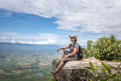 Woman sitting on rock against sky