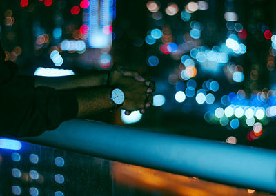 Cropped hands of man in balcony on railing at night