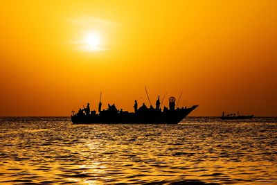 Silhouette fishermen on boat in sea against orange sky