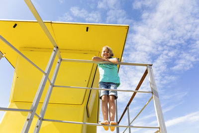 Happy boy standing on railing in front of yellow lifeguard hut