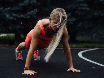 Young beautiful blond fitness model with long hair in neon orange activewear doing stretching 