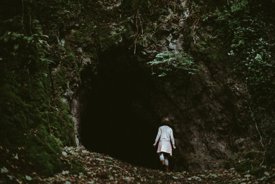 Young girl standing at cave opening in a wooded area