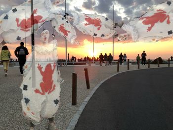 Rear view of people standing on street against sky at sunset