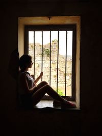 Side view of woman looking through window at home