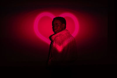 African american woman in trendy fur coat looking over the shoulder at camera while standing near dark wall with bright neon love sign