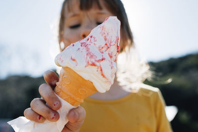 Low angle view of girl eating ice cream cone while standing against sky at park during sunny day