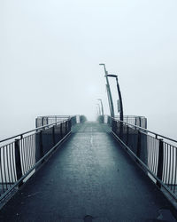 Empty footbridge in foggy weather against sky
