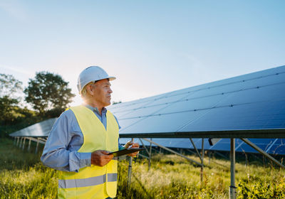 Rear view of engineer standing on field against clear sky