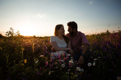 Young couple on field against sky during sunset