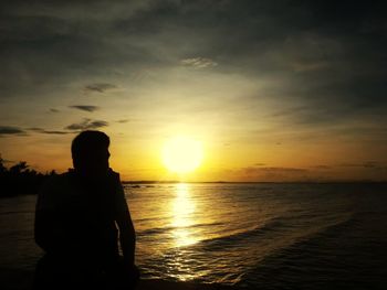 Rear view of silhouette man on beach against sky during sunset