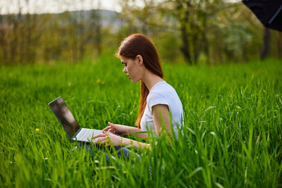 Young woman using mobile phone while sitting on grassy field