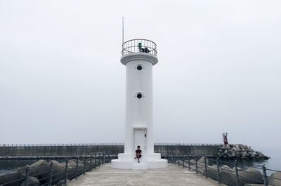 People on lighthouse by sea against clear sky
