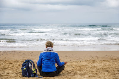 Woman sitting on the beach practicing meditation observing the horizon of the stormy sea. 