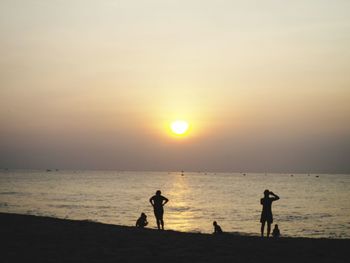Silhouette people on beach against sky during sunset