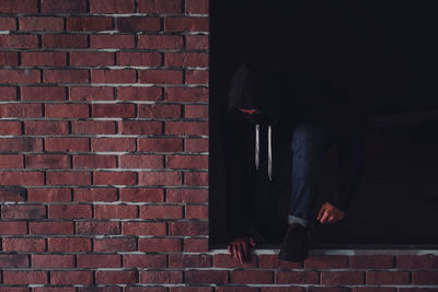 Low section of man sitting by brick wall