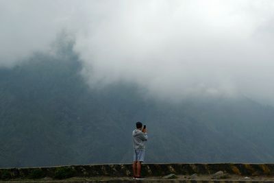 Rear view of woman standing on mountain in foggy weather