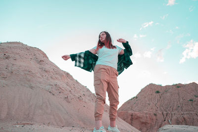 Portrait of young woman standing on rock against sky