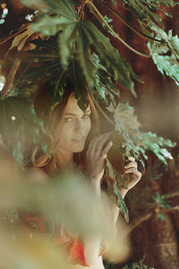 Portrait of young woman standing by tree