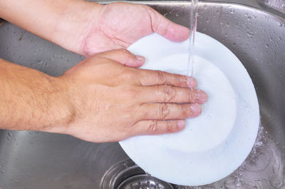 Cropped image of hands cleaning plate in kitchen sink