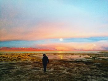 Rear view of silhouette man on beach against sky during sunset