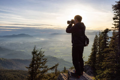 Man photographing on mountain against sky during sunset