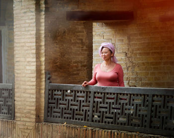 Woman standing by railing against brick wall