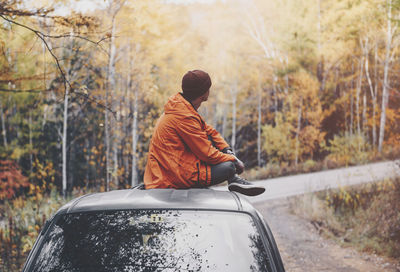 Side view of man sitting on car in forest during autumn