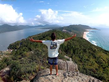 Rear view of people standing on mountain by sea against sky