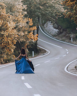 One young woman in blue dress walking on highway trough forest