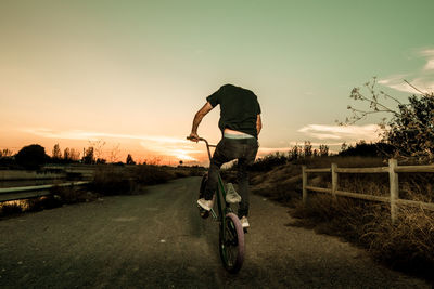 Man performing stunt with bicycle against sky during sunset