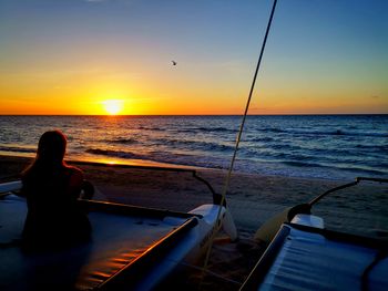 Rear view of woman sitting on sea against sunset sky