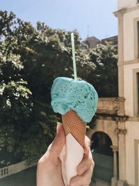 Cropped hand holding ice cream cone against trees