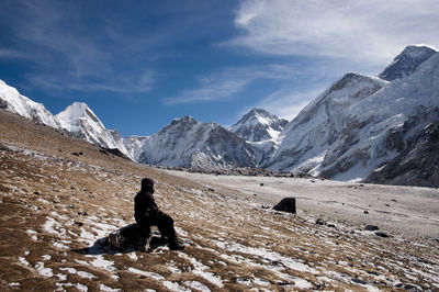 Man sitting on snowcapped mountain against sky