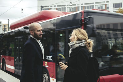 Business people talking on sidewalk by bus in city