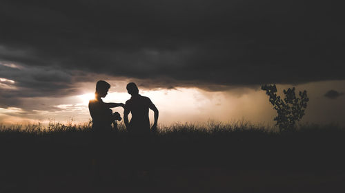 Silhouette men on field against sky during sunset