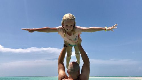 Side view of shirtless father holding girl in sea against sky