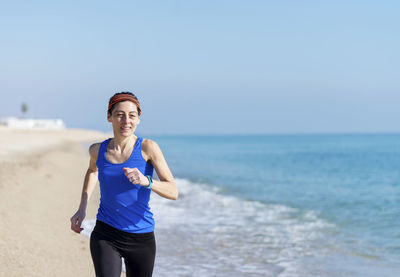 Woman running at beach against clear blue sky