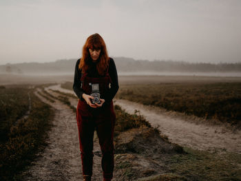 Woman holding camera standing on field