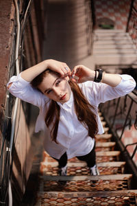 High angle portrait of young woman with arms raised standing on staircase