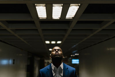 Male professional with eyes closed standing under illuminated light in subway