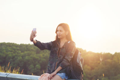 Young woman using smart phone against clear sky