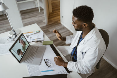 High angle view of male pediatrician greeting patients over video call on laptop at healthcare center