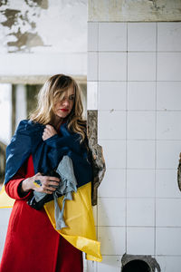 Woman holding ukrainian flag against wall