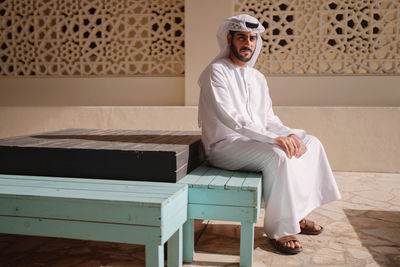 Portrait of arab man wearing dishdash kandura sitting down in a traditional bench