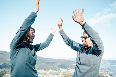 Smiling females with arms raised against sky