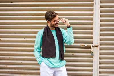 Young man using phone while standing against wall