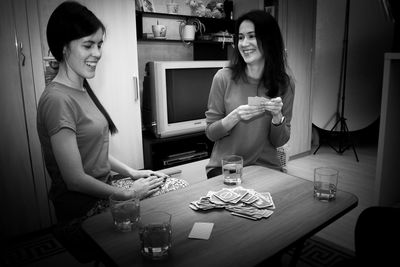 Smiling friends playing cards while sitting on table at home