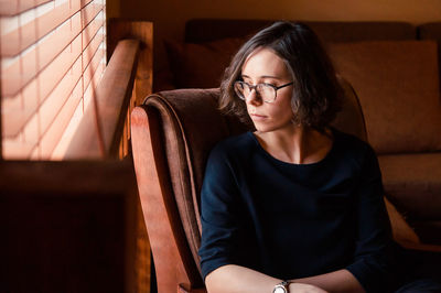 Woman looking away while sitting on chair at home