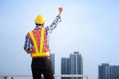 Rear view of engineer standing against buildings in city